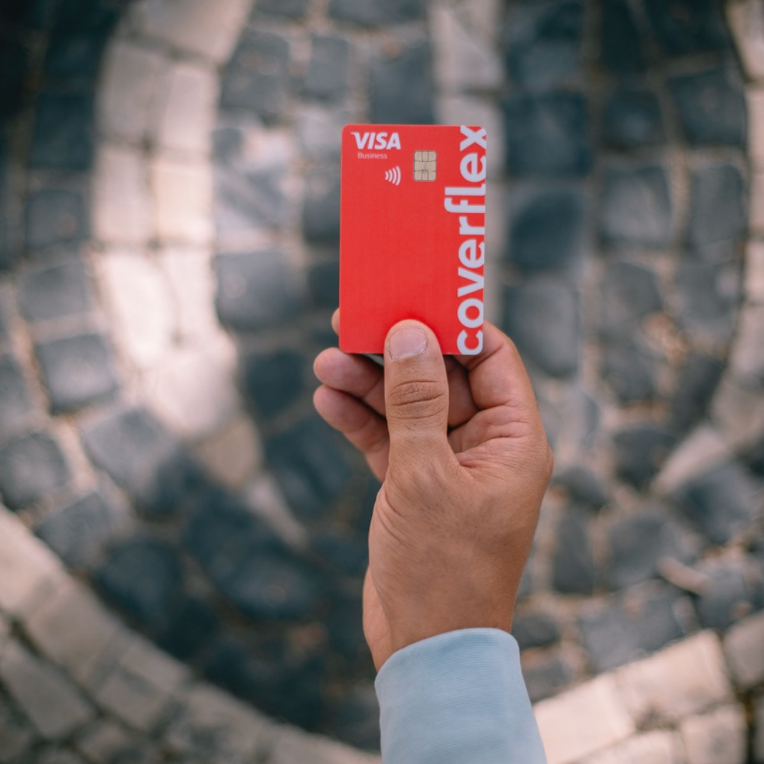 Una mano tiene una carta Coverflex rossa con logo Visa sopra uno sfondo in pietra.
